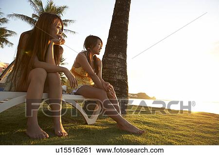 Stock Image - Young Women sitting on bench smiling, Guam, USA. Fotosearch