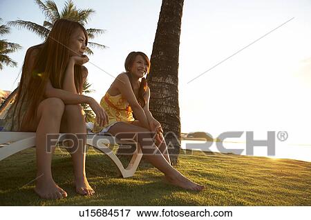 Stock Photo - Young Women sitting on bench smiling, Guam, USA. Fotosearch