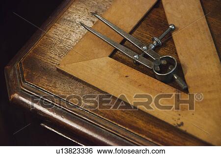 Stock Photograph - Antique set square and pair of compasses on wooden table. Fotosearch