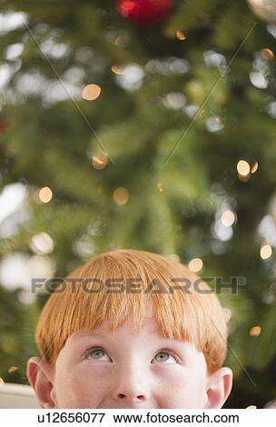 Stock Photo - Boy (8-9) by Christmas tree. Fotosearch