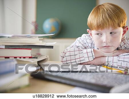Stock Image - Boy (8-9) sitting at crowded desk in classroom. Fotosearch