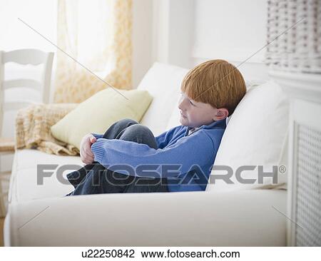 Boy (8-9) sitting on sofa View Large Photo Image Stock Image - Boy (8-9) sitting on sofa. Fotosearch