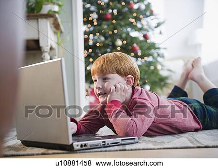 Stock Photo - Boy (8-9) wearing headphones, using laptop. Fotosearch