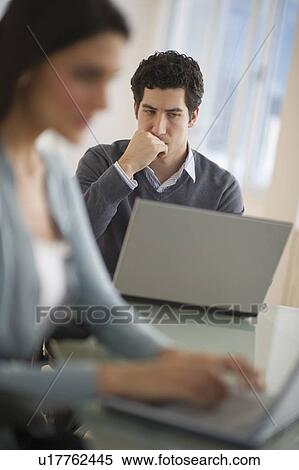 Stock Photography - Business man and woman using laptops in office. Fotosearch