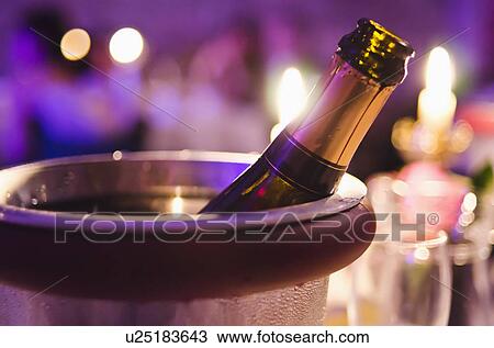 Stock Image - Champagne bottle cooling in ice bucket. Fotosearch
