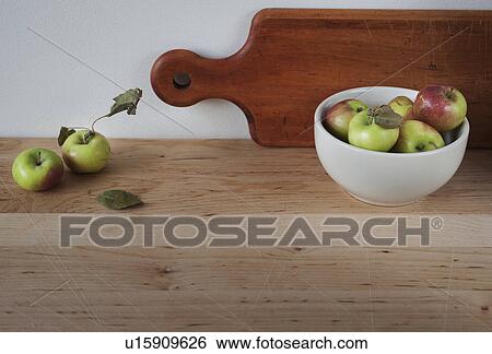 Stock Photograph - Close up of apples on table with bawl and cutting board. Fotosearch