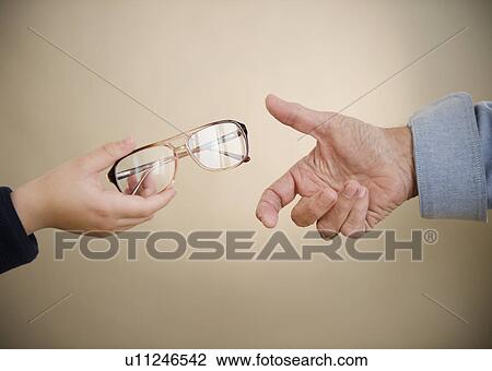 Stock Image - Close up of hands of grandfather and grandson (8-9) with glasses. Fotosearch