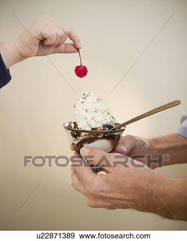 Stock Photo - Close up of hands of grandfather and grandson (8-9) holding icecreame and cherry. Fotosearch