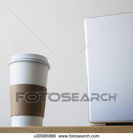 Coffee cup beside laptop in office View Large Photo Image Stock Photograph - Coffee cup beside laptop in office. Fotosearch