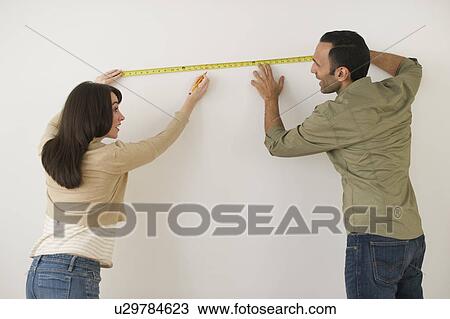 Couple measuring wall, studio shot View Large Photo Image Stock Image - Couple measuring wall, studio shot. Fotosearch