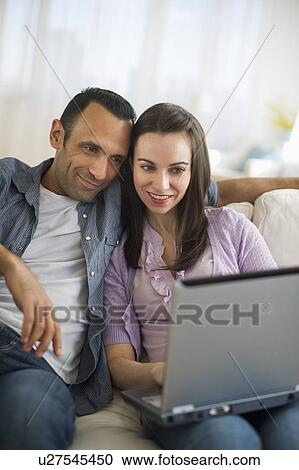 Stock Image - Couple sitting on sofa using laptop. Fotosearch