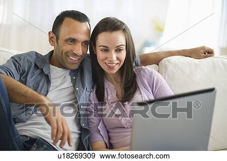 Couple sitting on sofa using laptop View Large Photo Image Stock Photo - Couple sitting on sofa using laptop. Fotosearch
