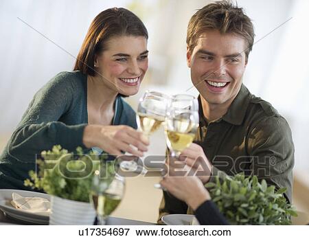 Stock Photo - Couple toasting with white wine with third party in background. Fotosearch