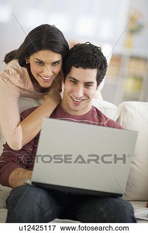 Stock Photo - Couple using laptop on sofa. Fotosearch