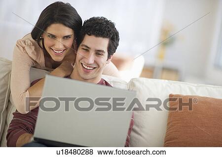 Stock Photo - Couple using laptop on sofa. Fotosearch