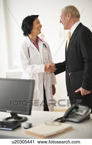 Stock Image - Female doctor shaking hands with hospital executive. Fotosearch