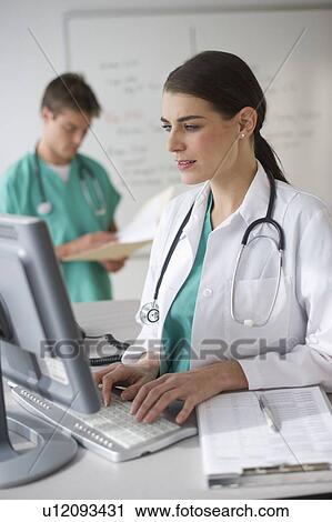 Female doctor working on computer with surgeon in background View Large Photo Image Stock Image - Female doctor working on computer with surgeon in background. Fotosearch