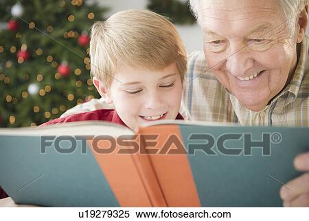 Stock Photography - Grandfather and grandson (8-9) reading book. Fotosearch