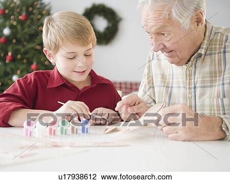 Stock Image - Grandfather and grandson (8-9 years) painting model airplane. Fotosearch