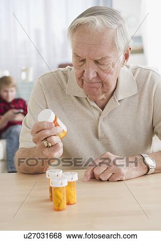Grandfather holding pill bottle, grandson (8-9) in background View Large Photo Image Stock Photo - Grandfather holding pill bottle, grandson (8-9) in background. Fotosearch