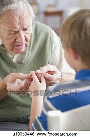 Grandfather stocking Band-Aid to grandson's (8-9) finger View Large Photo Image Stock Photograph - Grandfather stocking Band-Aid to grandson's (8-9) finger. Fotosearch