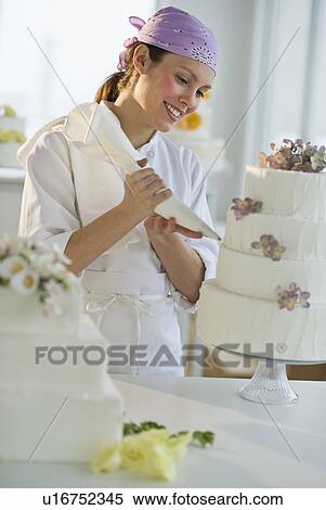 Stock Photography - Happy young woman decorating wedding cake. Fotosearch