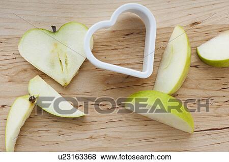 Stock Photo - Heart shaped apples with cutter on chopping board. Fotosearch