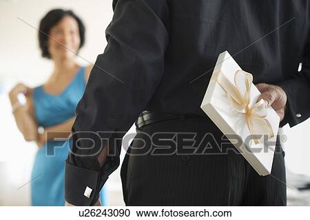 Stock Image - Man hiding gift box behind his back. Fotosearch
