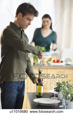 Man opening wine while woman is preparing food in background View Large Photo Image Stock Image - Man opening wine while woman is preparing food in background. Fotosearch