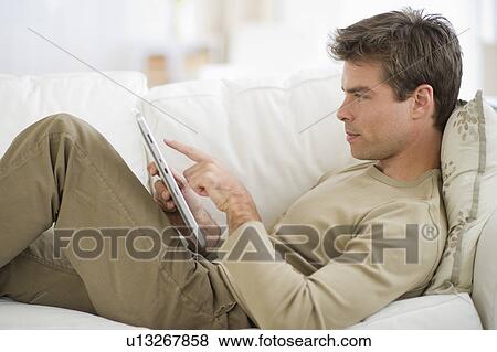 Man sitting on sofa, using digital tablet View Large Photo Image Stock Photo - Man sitting on sofa, using digital tablet. Fotosearch