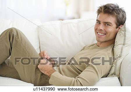 Stock Image - Man sitting on sofa with digital tablet. Fotosearch