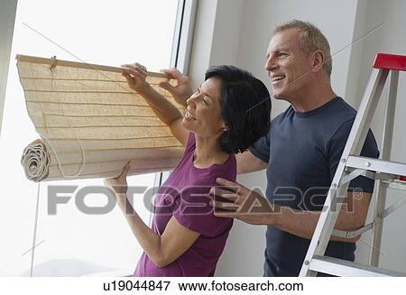Stock Photo - Mature couple hanging blinds. Fotosearch
