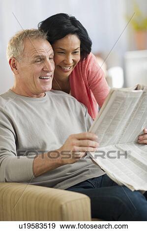Mature couple sitting in armchair, reading newspaper View Large Photo Image Stock Photo - Mature couple sitting in armchair, reading newspaper. Fotosearch