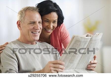 Mature couple sitting in armchair, reading newspaper View Large Photo Image Stock Photograph - Mature couple sitting in armchair, reading newspaper. Fotosearch
