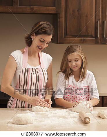 Stock Photo - Mother and daughter (10-11) kneading dough in kitchen. Fotosearch