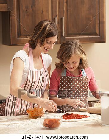 Stock Image - Mother and daughter (10-11) preparing pizza in kitchen. Fotosearch