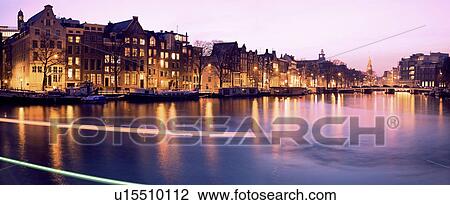 Stock Image - Netherlands, Amsterdam, Illuminated buildings by canal. Fotosearch