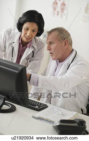 Pair of mature doctors discussing in front of computer View Large Photo Image Picture - Pair of mature doctors discussing in front of computer. Fotosearch