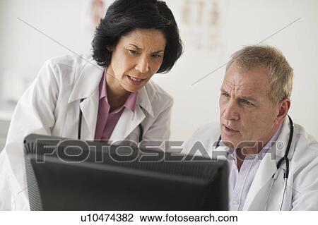 Stock Image - Pair of mature doctors discussing in front of computer. Fotosearch