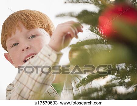 Stock Image - Portrait of boy (8-9) preparing Christmas tree. Fotosearch
