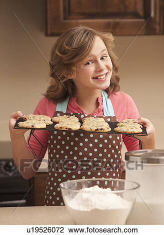 Stock Image - Portrait of girl (10-11) holding biscuits in kitchen. Fotosearch
