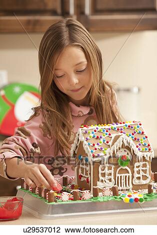 Stock Image - Portrait of girl (6-7) making gingerbread house. Fotosearch