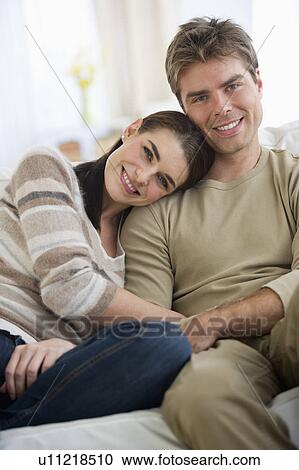 Stock Image - Portrait of happy couple sitting on sofa. Fotosearch