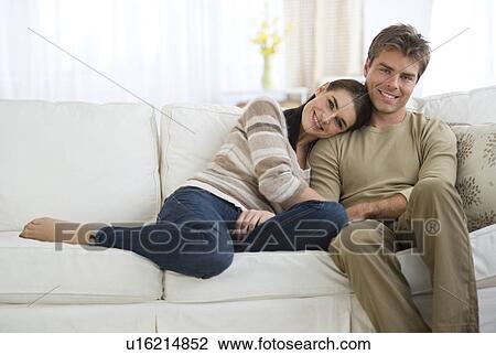 Stock Image - Portrait of happy couple sitting on sofa. Fotosearch
