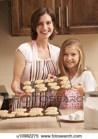Stock Photography - Portrait of mother holding biscuits with daughter (10-11) in kitchen. Fotosearch
