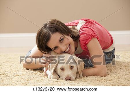 Stock Image - Portrait of woman embracing Labrador on carpet. Fotosearch