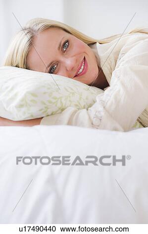 Stock Image - Portrait of woman lying on bed. Fotosearch