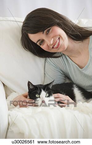 Stock Image - Portrait of woman with cat on sofa. Fotosearch