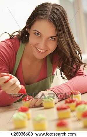 Stock Photo - Portrait of young woman decorating cupcakes in kitchen. Fotosearch