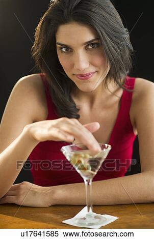 Stock Photography - Portrait of young woman drinking martini, studio shot. Fotosearch